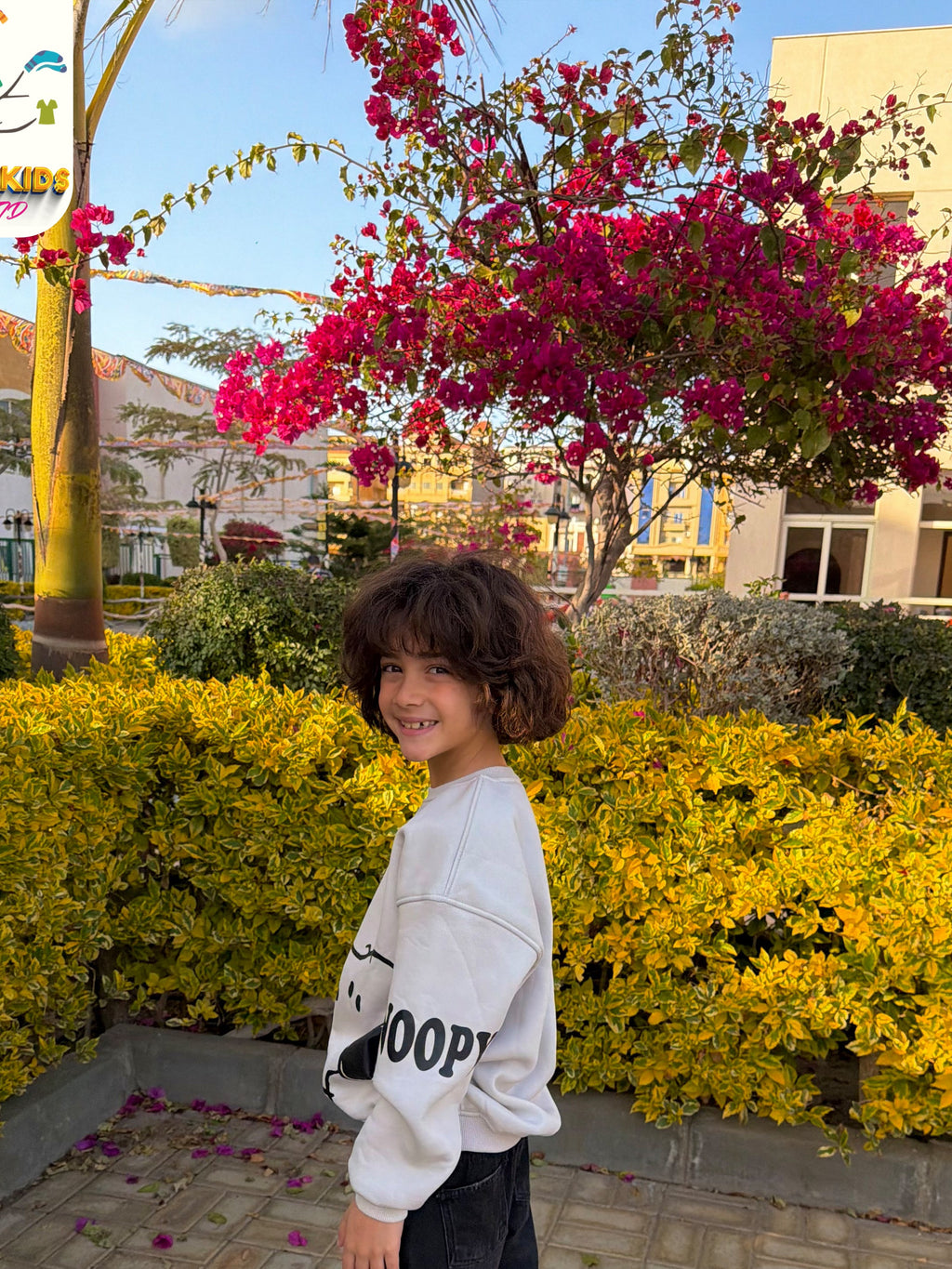 Child standing in a garden with flowering bushes and trees