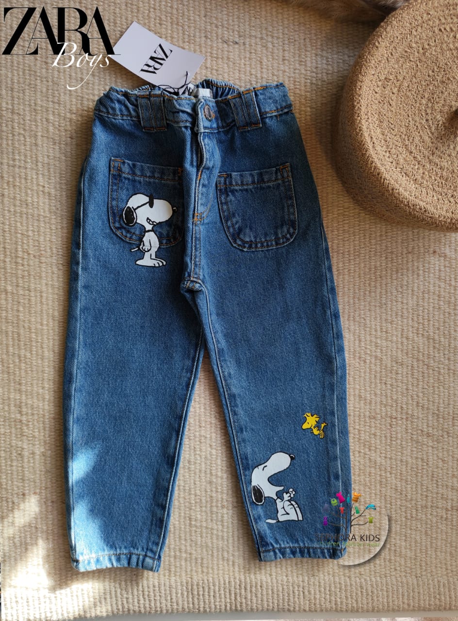 Children's blue jeans with Snoopy designs on a textured surface, featuring Zara branding.