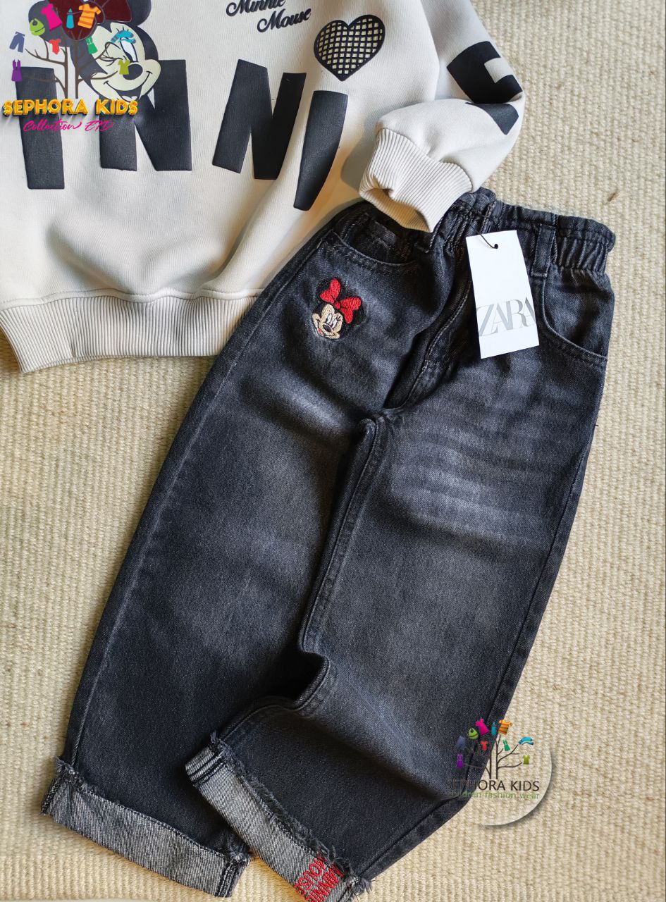 Children's black jeans with a white sweatshirt on a textured surface, featuring a brand tag.